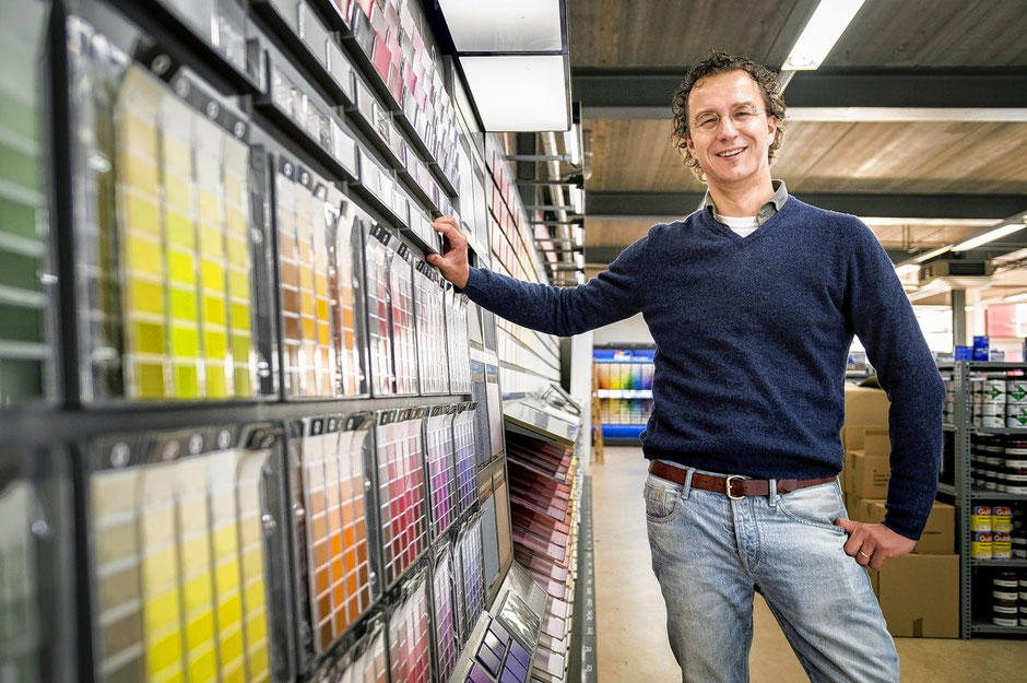 Adriaan Guldie staat bij een wand met stalen in zijn verfwinkel